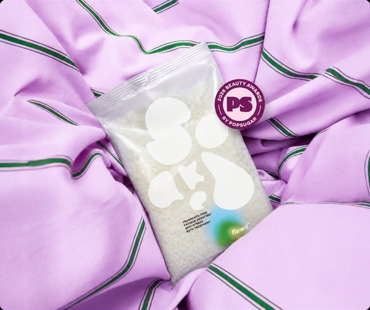 Flewd fragrance-free Fatigue Defeating stresscare bath soak clear pouch on a lilac striped sheet with a PopSugar award badge